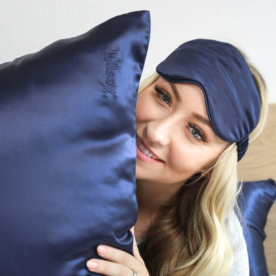Woman wearing Blissy pure mulberry silk sleep mask in calming blue while resting in bed