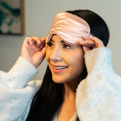 Model sleeping peacefully wearing Blissy pure mulberry silk sleep mask in rose gold