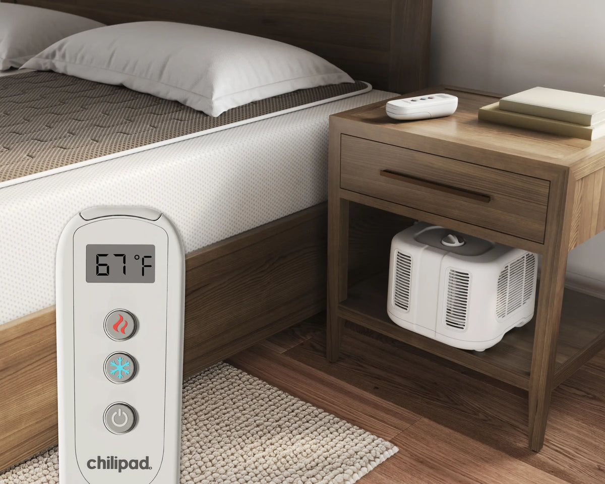 Chilipad electric blanket control panel next to a bed with an air conditioner underneath a nightstand.