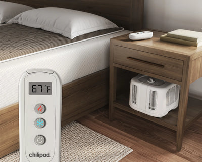 Chilipad electric blanket control panel next to a bed with an air conditioner underneath a nightstand.