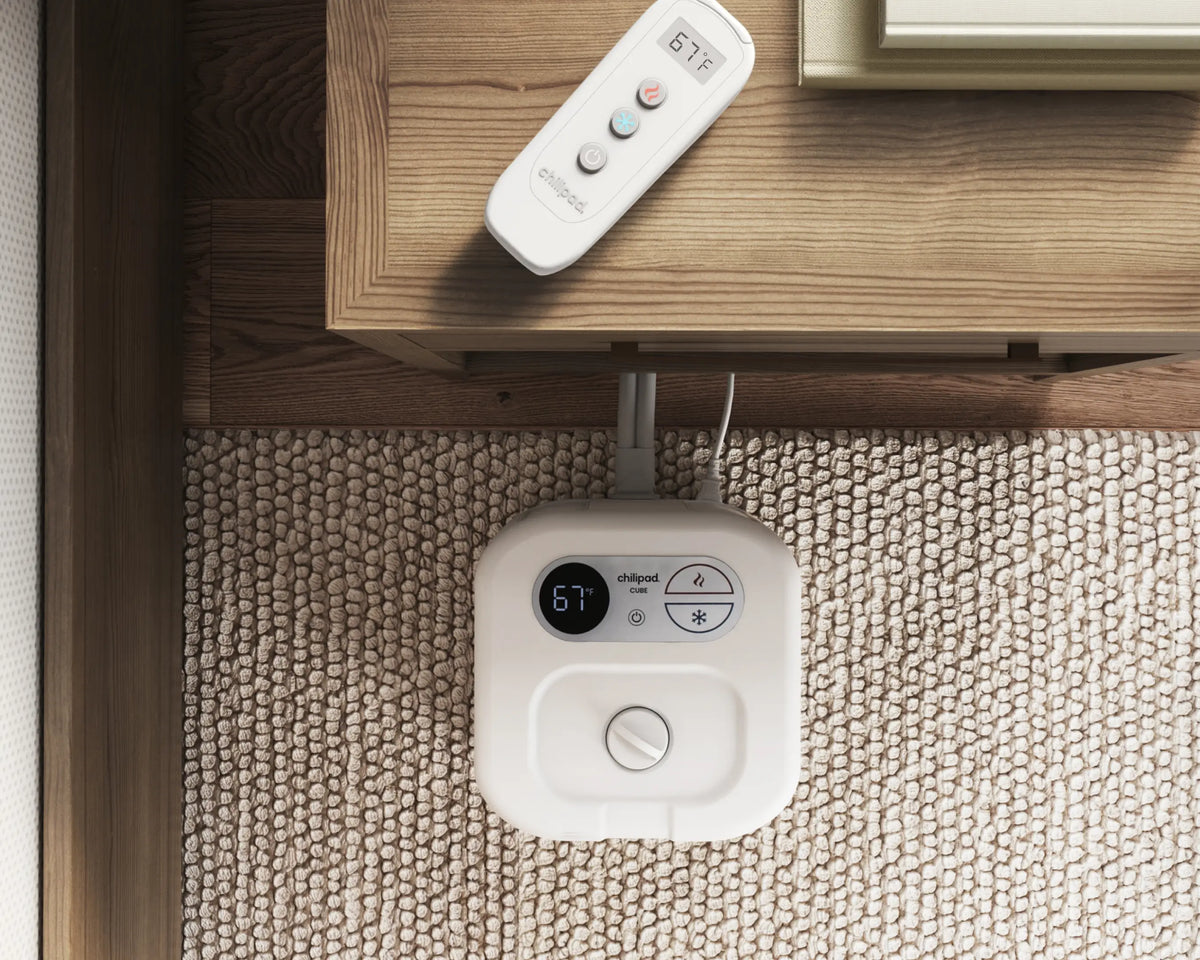 White robot vacuum cleaner on a carpeted floor with a remote control on a wooden table.