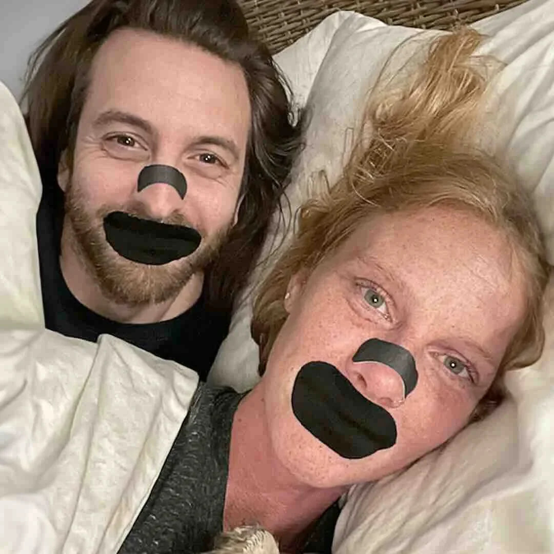 Couple in bed smiling while using Hostage Nose Strips for peaceful, quiet sleep