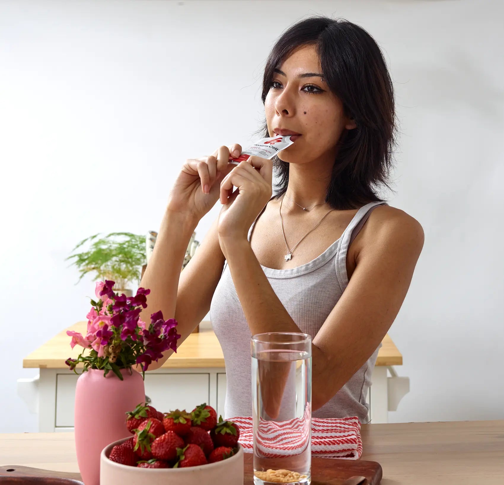 Woman eating a snack with strawberries and a glass of water on a table. HealthCell packet.