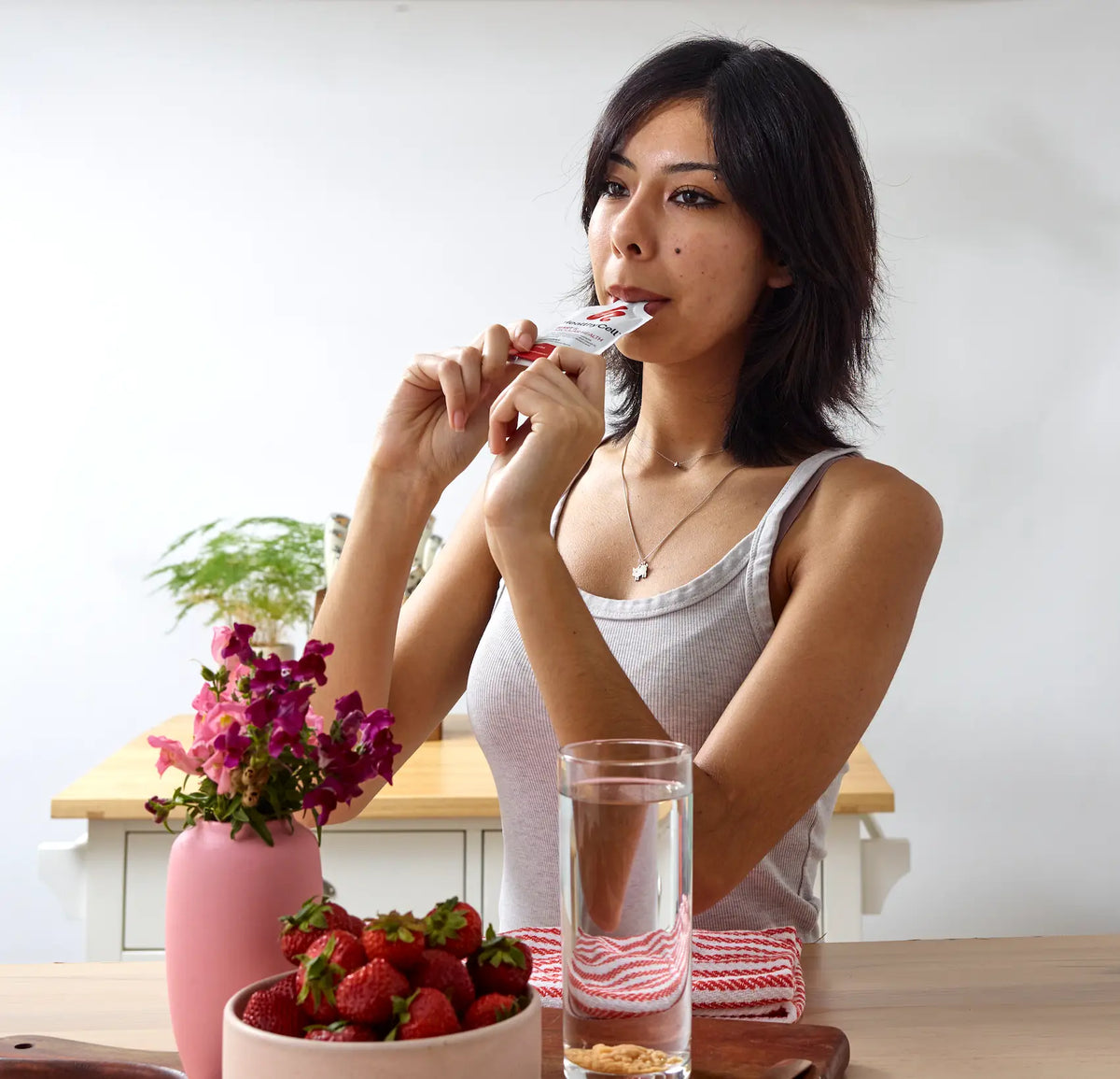 Woman eating a snack with strawberries and a glass of water on a table. HealthCell packet.