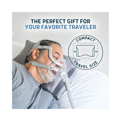 A man wearing a compact travel-size CPAP mask and hose while resting in bed, with promotional text reading 'THE PERFECT GIFT FOR YOUR FAVORITE TRAVELER' and a circular badge labeled 'COMPACT TRAVEL SIZE'.