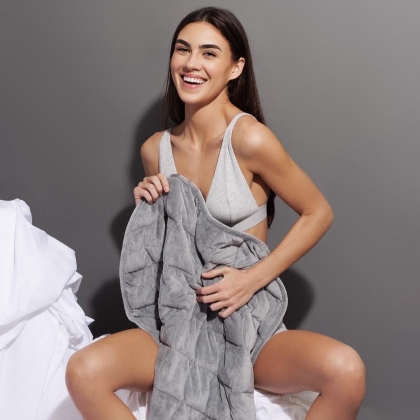 Model resting under Nodpod BODY weighted blanket on sofa experiencing soothing relaxation