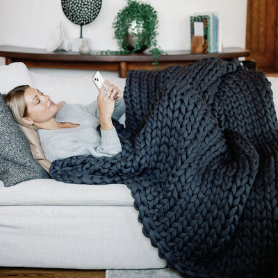 Nuzzie open-loop chunky knit weighted blanket in charcoal gray draped across modern couch