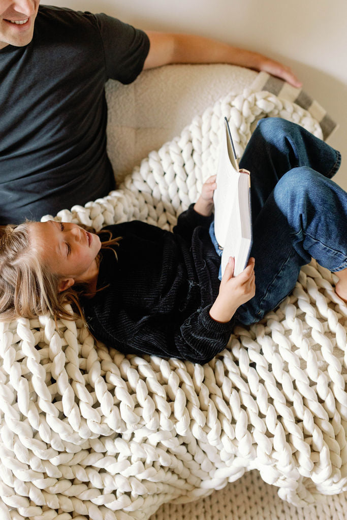 Nuzzie knit weighted blanket in Cream, draped over a person relaxing