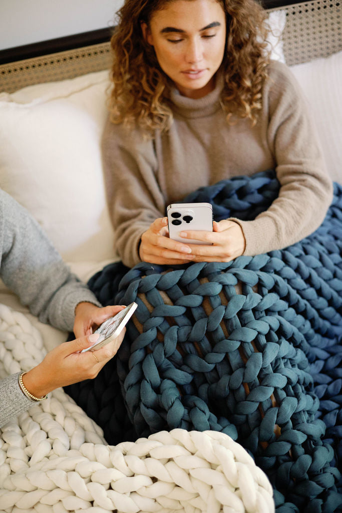 Nuzzie knit weighted blanket in Dusty Blue, used while lounging on a couch