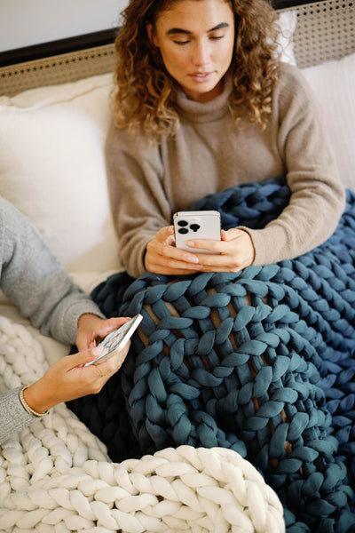 Nuzzie knit weighted blanket in Dusty Blue, used while lounging on a couch