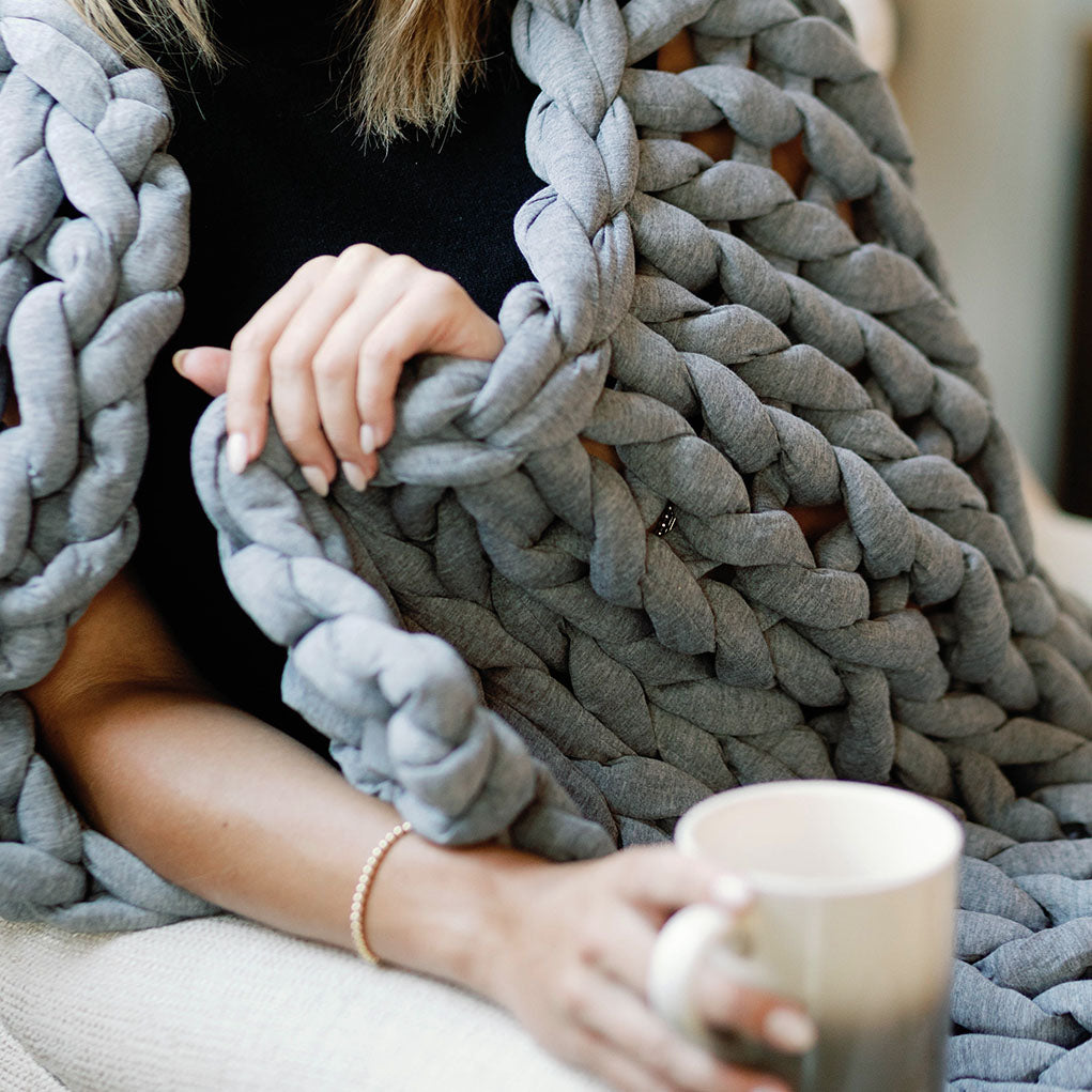 Person warmly wrapped in Nuzzie chunky knit weighted blanket in heather gray