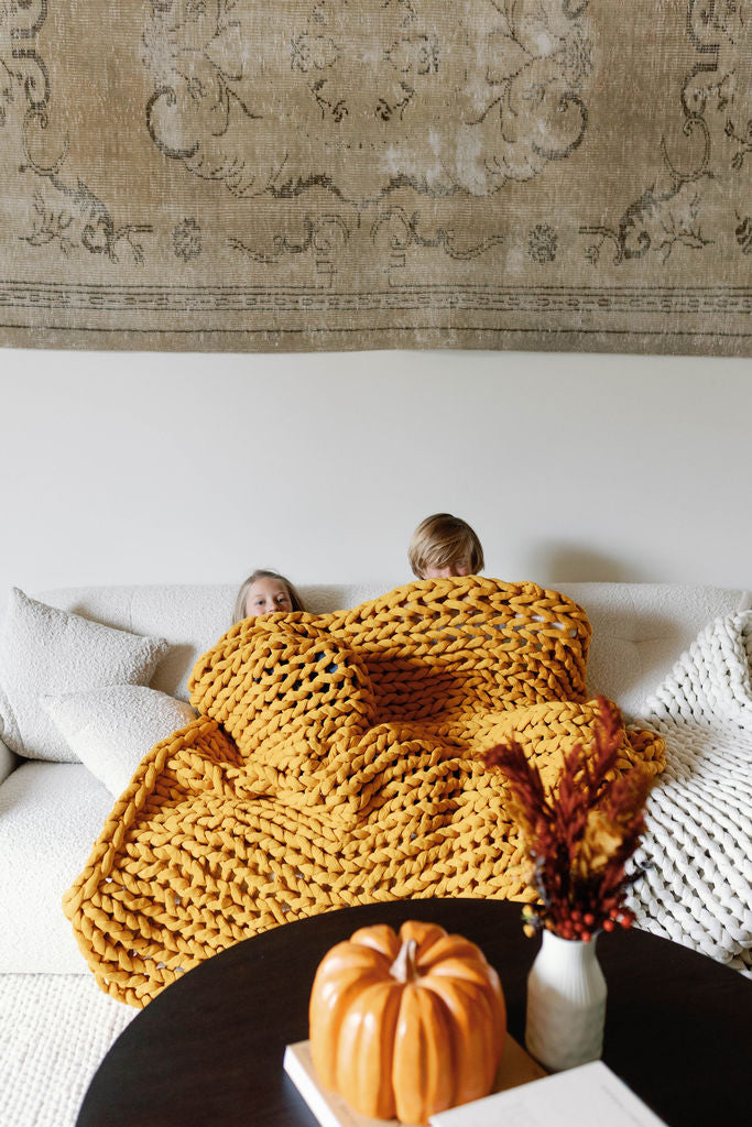 Nuzzie knit weighted blanket in Marigold, with kids snuggled underneath