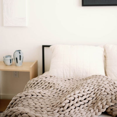 Nuzzie knit weighted blanket in Taupe, laid across a mattress