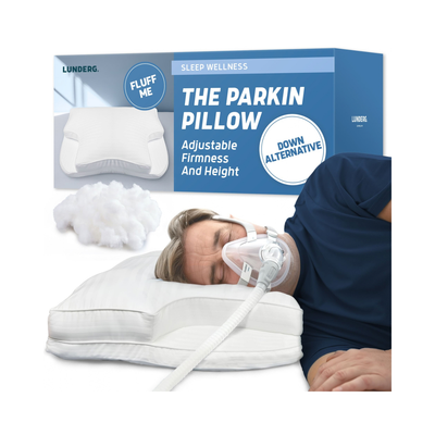 Lunderg The Parkinson Pillow product packaging and a demonstration photo of a man sleeping peacefully on the adjustable white pillow with a breathing tube, with loose white filling material shown in front.
