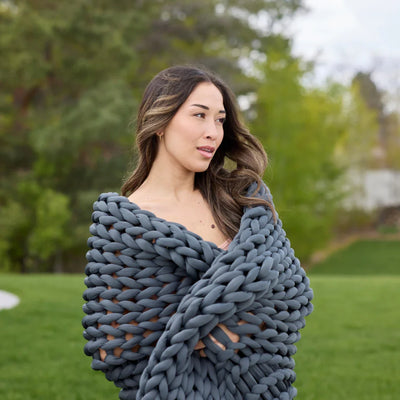 Person relaxing on couch under breathable Nuzzie Ice Knit weighted blanket in northern grey