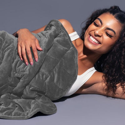 Woman lounging comfortably wrapped in Nodpod BODY weighted blanket in elephant gray