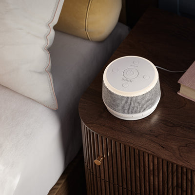 Yogasleep Dohm Nova sound machine with warm glow night light illuminated on bedside table