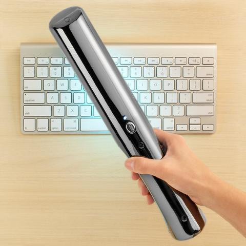 Lumin Wand cordless UV-C sanitizer being waved across a computer keyboard to eliminate germs